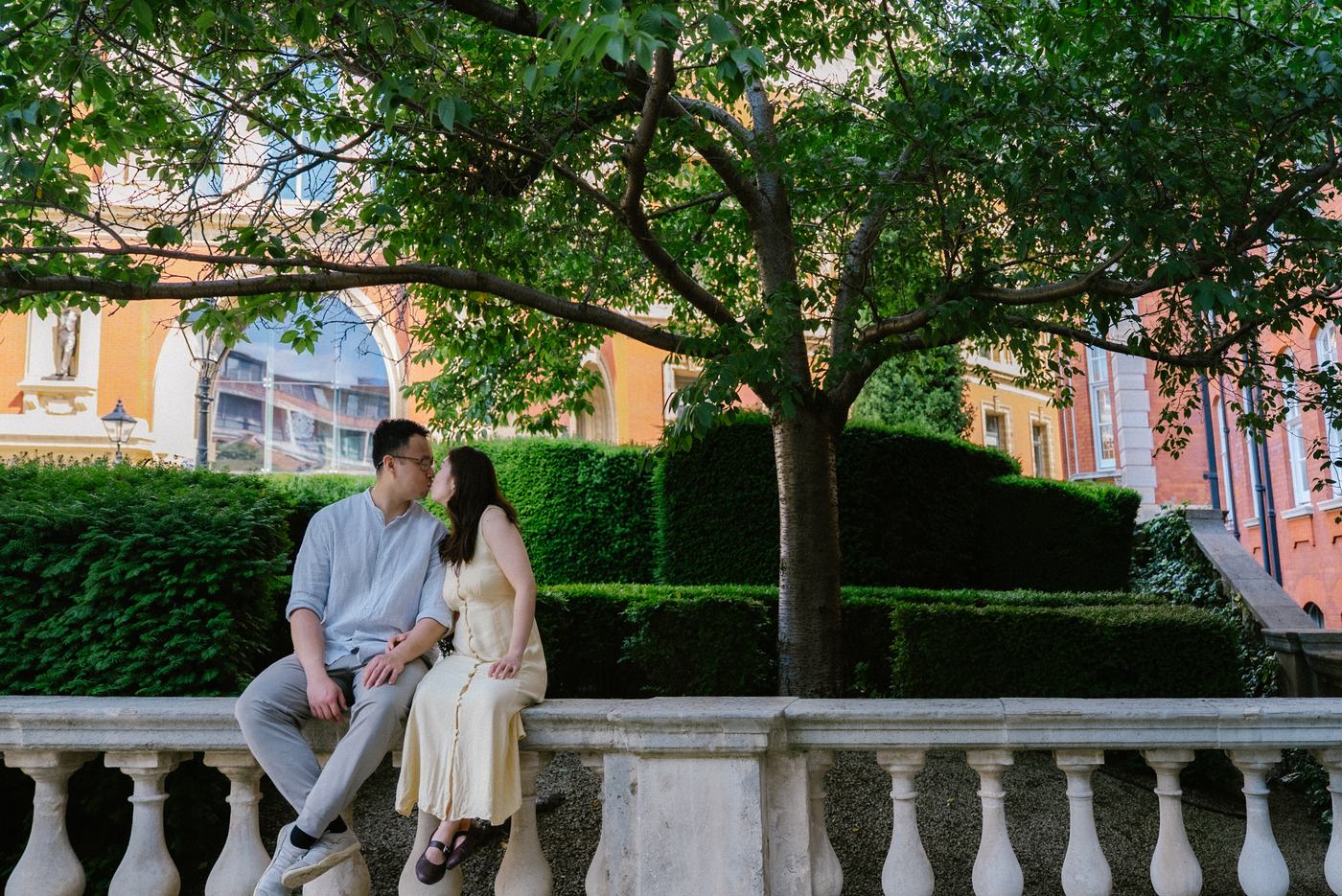 Couple sitting together on a stone balustrade under a tree