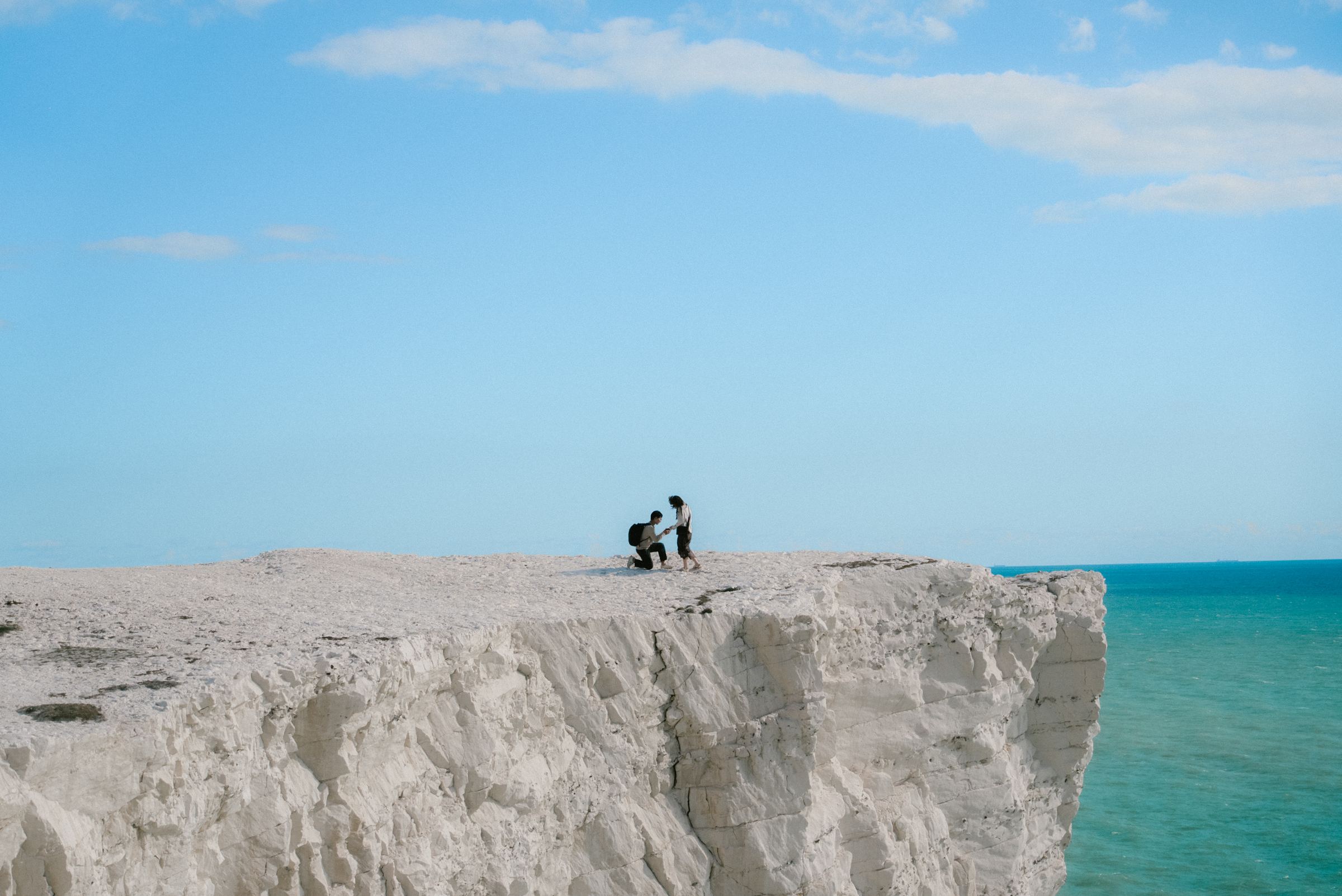 A tiny couple on the edge of the white Seven Sisters cliffs above a turquoise sea
