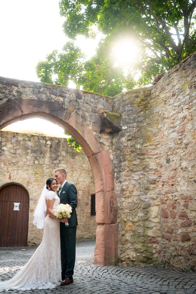 Newlyweds under a stone archway in the sun