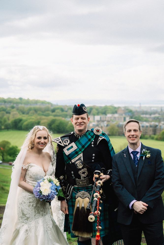 Bride and groom with a bagpiper on Arthur's Seat