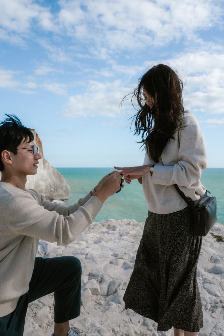 Man on one knee holding a ring on white cliffs