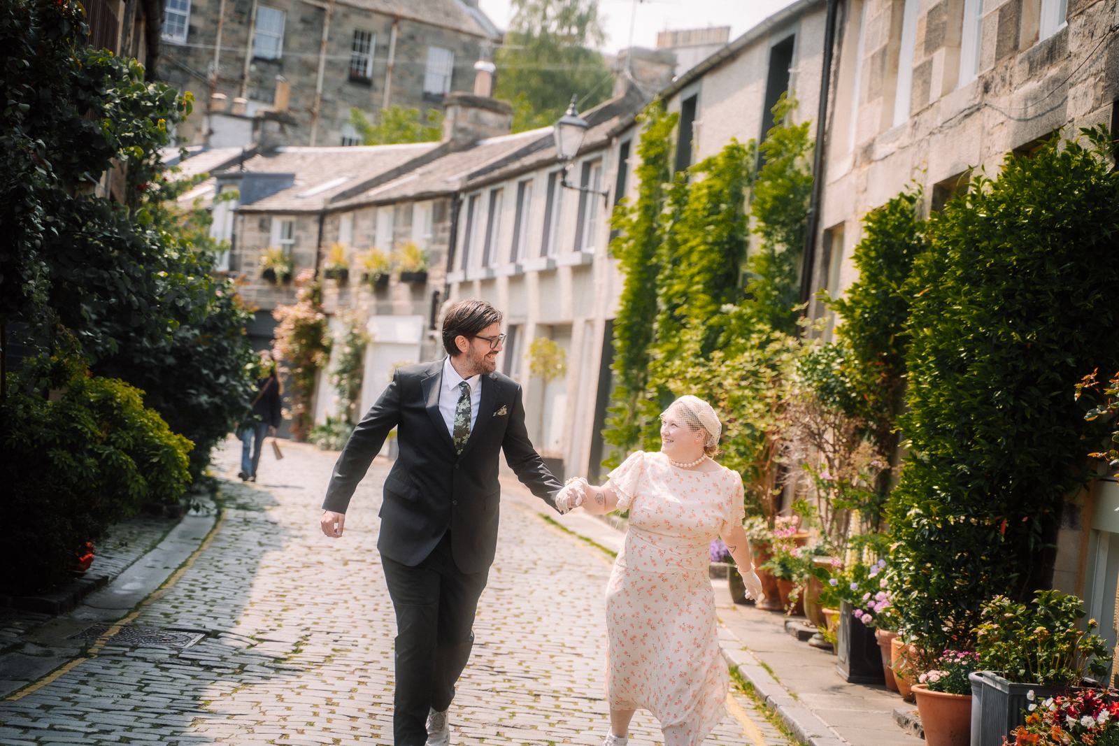 Newlyweds walking hand in hand down a cobbled lane