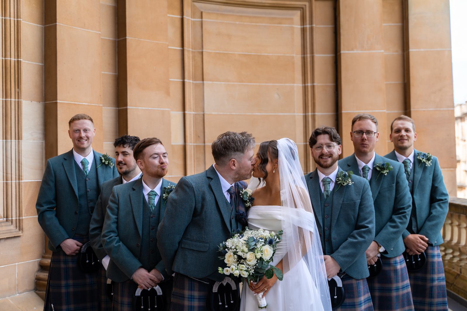 Groom and groomsmen in kilts cheering with the bride