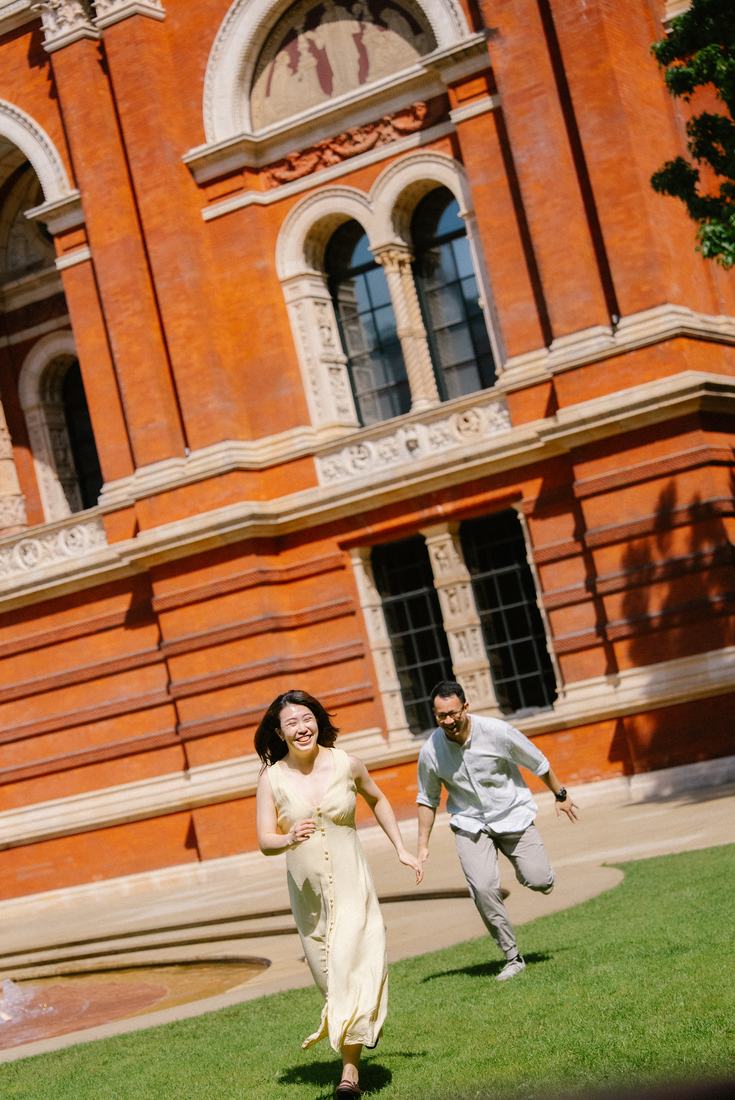 Couple running across a lawn in front of a red brick museum